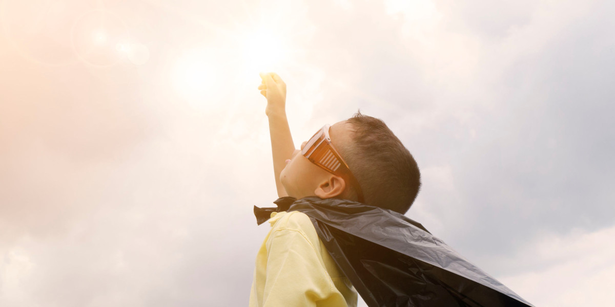 little boy in a cape with sunglasses reaching up to sun